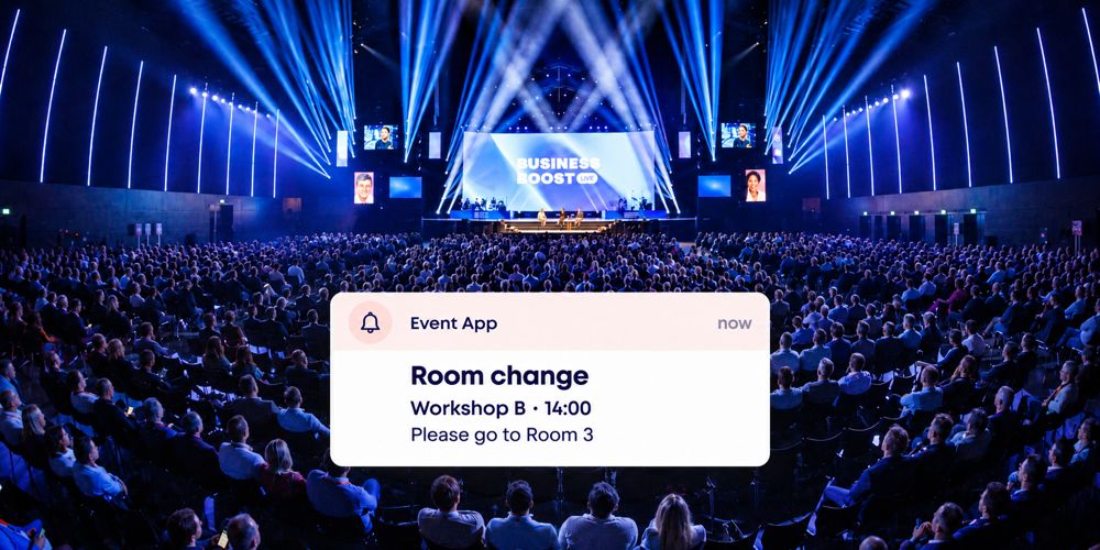 Conference audience under blue stage lighting with an Event App notification about a room change for Workshop B.