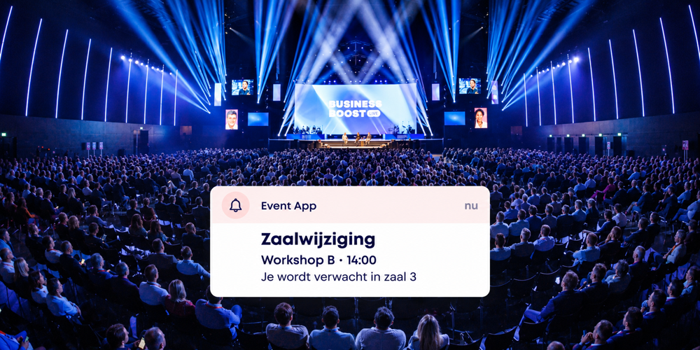 Congreszaal met blauw podiumlicht en een melding in de Event App over een zaalwijziging voor workshop B.